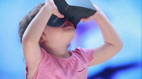 Virtual reality game. The little girl with surprise and pleasure uses head-mounted display.