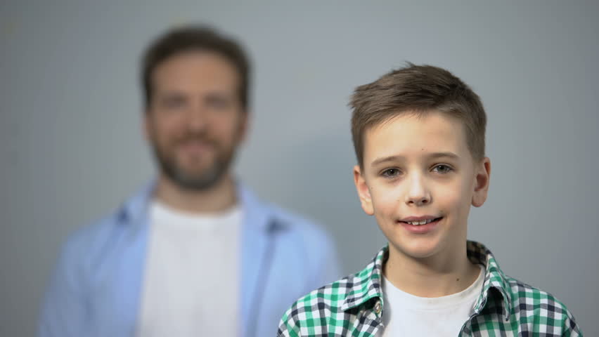 Boy smiling at camera, father standing on background, family care and support