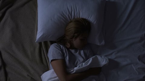 Pretty woman turning in her bed feeling discomfort, bad quality of mattress