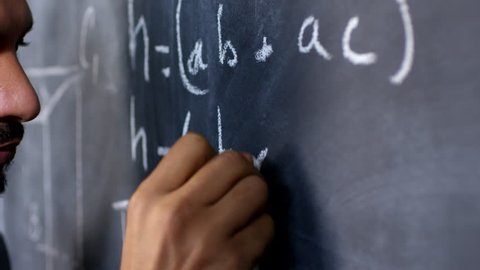 Handheld tracking shot with close up of male university professor writing math formula on chalkboard