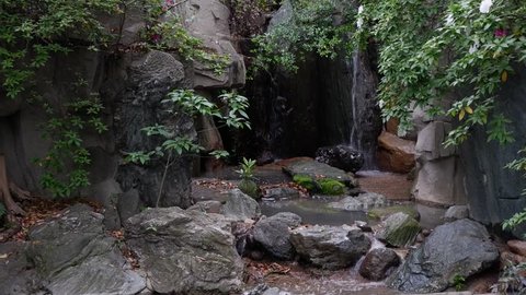 WATERFALL BETWEEN LEAVES AND ROCKS IN SMALL SPRING GARDEN