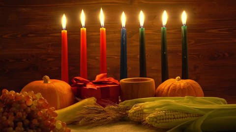 Kwanzaa festive concept with burning seven candles red, black and green decorated corns, grapes, bananas, gift boxes, pumpkin, bowl and fruits