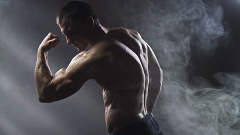 Bodybuilder posing in studio on a dark background. Handsome shirtless athletic man