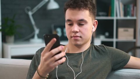 Young boy is enjoying the music in his headphones and texting someone through an app on his phone. Stay at home.