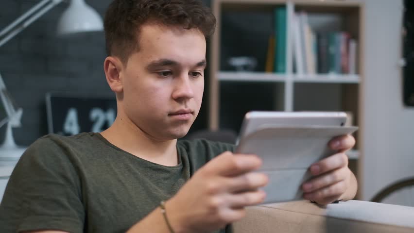 Young teenage boy is concentrated on his tablet, close-up front view in the room
