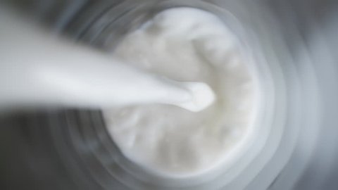 Top view of milk being poured in a glass on dark color table, close up of pouring milk on black background, slow motion