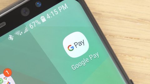 MONTREAL, CANADA - May 2019 : Closeup shot of a finger opening Google Pay app on a smartphone touch screen. Top view of the desk.