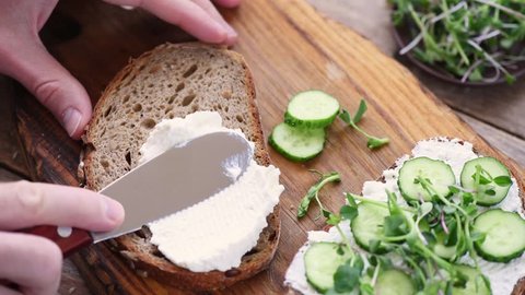Making healthy sandwich with cottage cheese and cucumber. Person spreading cream cheese on rye bread
