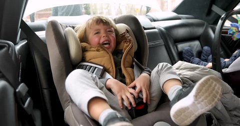 Closeup crying boy with worried stressed expression in child safety seat in car interior