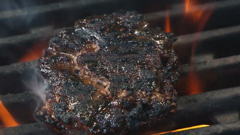 Chief cooked meat for a burger on the grill turning using the spatula slow motion. Fire is burning and juicy steak with stripes are become to be ready. Oil roast filet, unhealthy but fast food concept