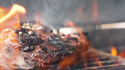 Delicious juicy meat steaks cooking on the grill on fire. Aged prime rare roast grilling tenderloin fresh juicy beef filet with lines slow motion. Grill, tasty beefsteak close up