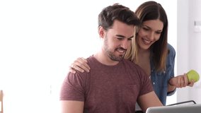 Video of beautiful lovely young couple using their laptop and talking in the kitchen at home.