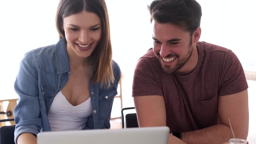 Video of beautiful lovely young couple using their laptop and talking in the kitchen at home.