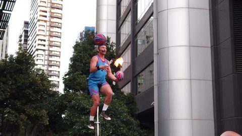 Melbourne Australia - 04 10 2019: an entertainer perform tricks with basketball and flame torch on unicycle in front of a cheering crowd in Melbourne street along yarra river 