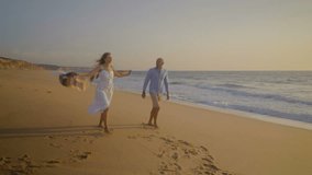 Happy couple running on beach at sunset. Full length view of excited young couple in love running together on sand at seaside. Togetherness concept
