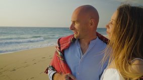 Beautiful young couple looking at seaview. Happy young couple wrapped in plaid standing on beach and kissing. Togetherness concept