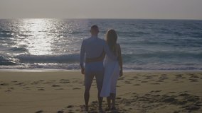 Young couple in love looking at beautiful ocean. Back view of man and woman embracing and standing on sandy beach at sunset. Nature concept
