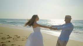 Happy couple in love having fun on beach. Smiling young man and woman holding hands and turning around on sandy beach at seaside. Love concept