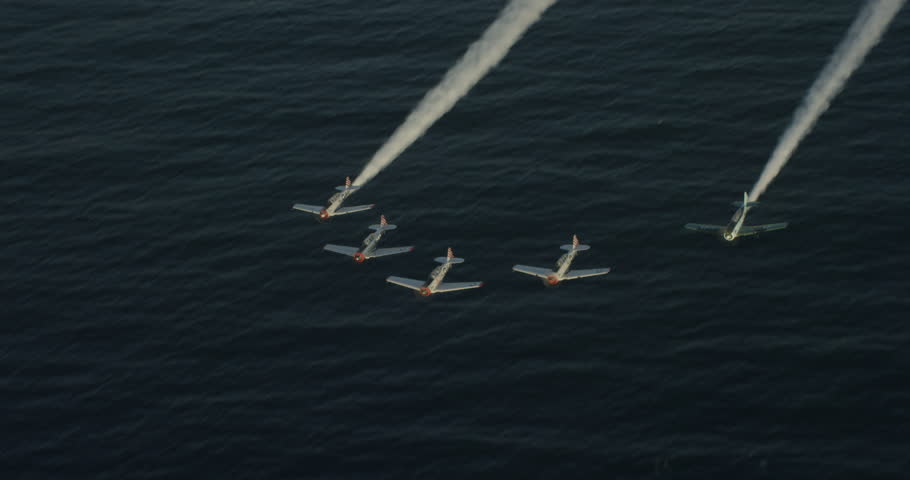 Helicopter aerial birds eye view shot of small skywriting planes above ocean, overcast day
