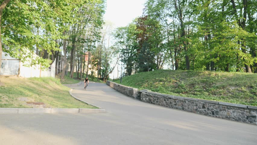 Man cycling. Male on bicycle. Professional strong skinny bike rider descending on curvy road wearing black jersey and shorts. Cyclist going down the hill. Slow motion