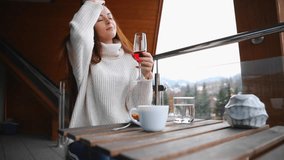 Young girl in a sweater sitting on a balcony taking a glass of red wine to play with her long hairs