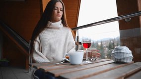 Young girl in sweater sitting on balcony taking glass of red wine and drinking during morning ceremony