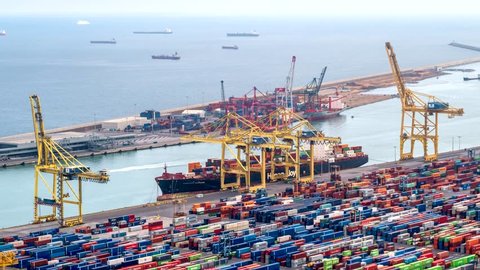 BARCELONA, SPAIN - APRIL 17, 2019: Aerial timelapse of ship unloading in Barcelona port terminal with straddle carrier trucks moving shipping containers. Zoom in effect