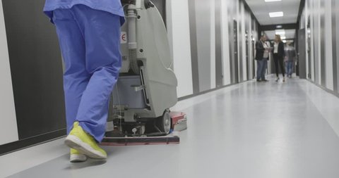 Professional maid cleaning and washing floor with machinery in industrial building