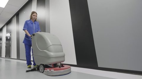 Female office cleaner using scrubber machine for cleaning and polishing floor