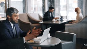 Modern businessman is communicating talking and gesturing using wireless earphones and laptop in cafe. Modern gadgets, technology and communication concept. - Powered by Shutterstock - Get 15% off with code: PIKWIZARD15