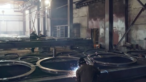 PAN shot of unrecognizable male workers welding and polishing round metal parts at fabrication facility Video de stock