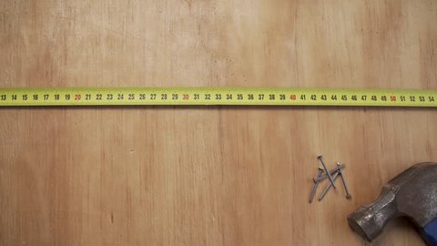 Tape measure a rolled out on wood surface as a hand with a pencil does measurement markings.