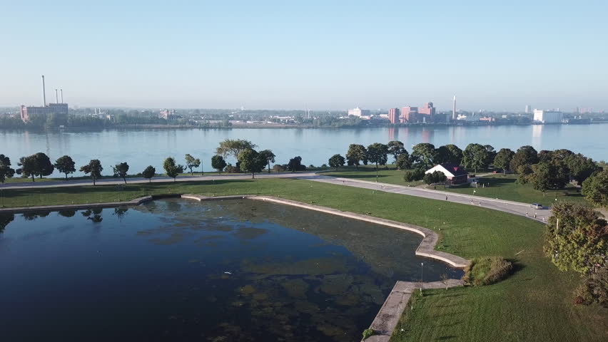 View of the Detroit skyline from Belle Isle on the Detroit river. Lake freighter passing by on a sunny summer day with blue sky. Aerial drone video of Michigan.