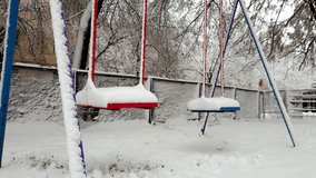 4k video of empty swings on playground covered in snow swaying by wind