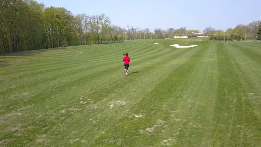 4K. Aerial. Woman runner run on green field. Camera down inclination  