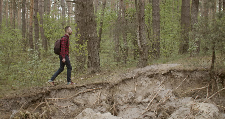 Sporty young man dressed in checked shirt walking in the pine forest