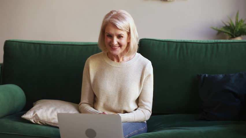 Happy older woman talking to webcam making distance video call on laptop sit on sofa, cheerful friendly middle aged lady enjoy online chat internet conversation looking at computer at home Royalty-Free Stock Footage #1029041525