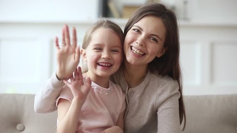 Happy family young mom and cute child daughter waving hands looking at camera make video call, mother with kid girl recording vlog talking to webcam laugh embrace communicate online in internet