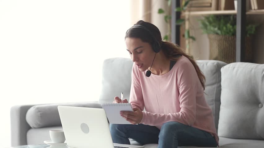Smiling young woman interpreter wearing headset talking on making notes, happy female online teacher tutoring teaching by distant video call, student e learning on web sitting on sofa at home Royalty-Free Stock Footage #1029041531