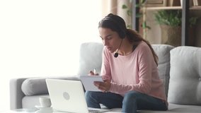 Smiling young woman interpreter wearing headset talking on making notes, happy female online teacher tutoring teaching by distant video call, student e learning on web sitting on sofa at home - Powered by Shutterstock - Get 15% off with code: PIKWIZARD15