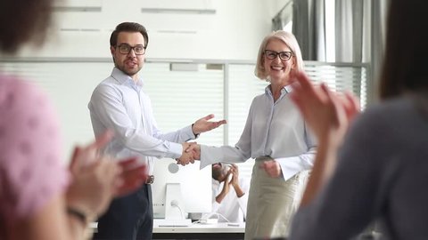 Happy manager boss praise old female employee for great professional achievement handshake loyalty member get team applause appreciation, proud mature worker promoted rewarded with respect handshake