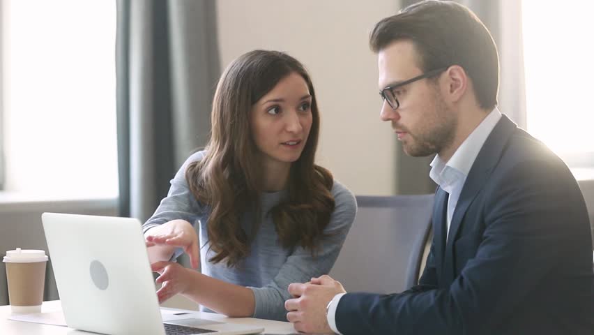 Female manager insurer consulting male customer with laptop at meeting, young saleswoman or mentor showing online presentation of deal benefits talking convincing client teaching intern sit at desk