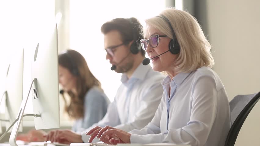 Older mature business woman wear wireless headset working in customer service support office, senior aged call centre agent operator using computer consulting client with request or complaint Royalty-Free Stock Footage #1029051452