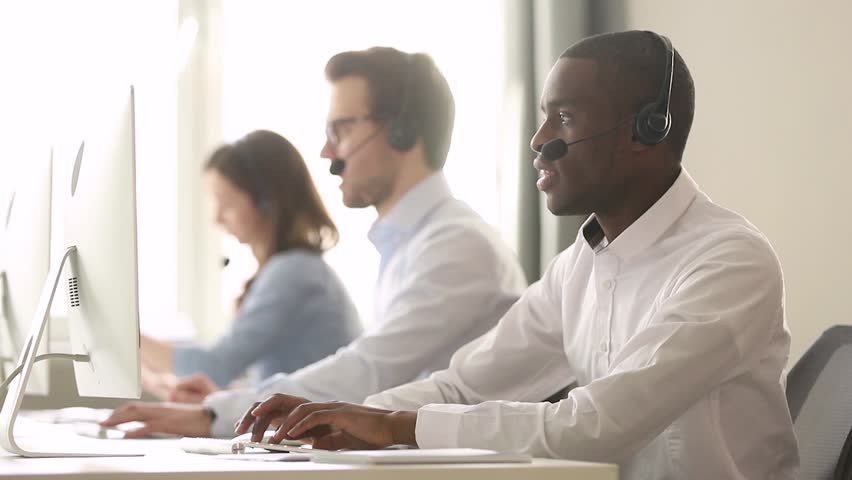 Focused african american call center agent wear wireless headset working on computer consulting customer, serious black male operator telemarketer use pc help client care support service on helpline Royalty-Free Stock Footage #1029051458