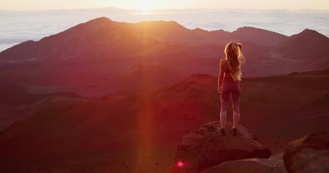 Young athletic woman raising her arms in joy while she watches an epic sunrise at the top of a mountain, breathtaking outdoor fitness moments in slow motion