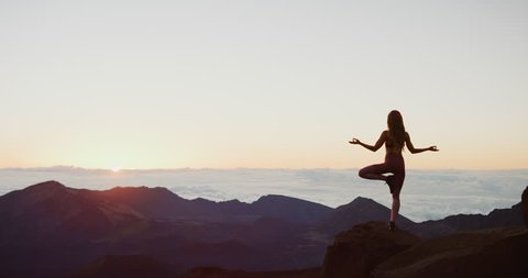 Young attractive woman doing yoga at sunrise on the top of a mountain, zen sunrise yoga pose silhouette