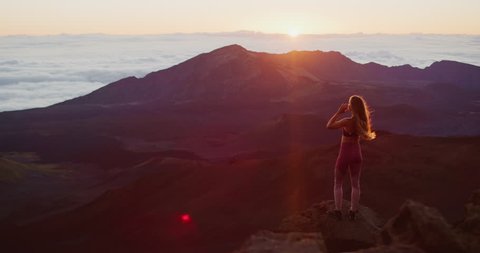 Young athletic woman raising her arms in joy while she watches an epic sunrise at the top of a mountain, breathtaking outdoor fitness moments in slow motion