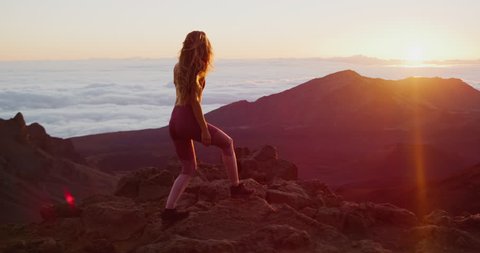 Young athletic woman walking on the top of a mountain and looking out at an epic sunrise, epic outdoor fitness in slow motion