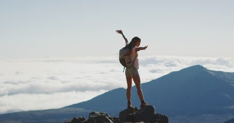 Young adventurous woman standing on the top of a mountain enjoying the view with her arms raised in the air, active summer hiking lifestyle