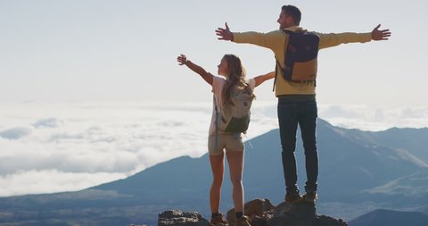 Young adventurous couple raising their arms in joy at the top of a mountain, amazing summer wilderness adventures